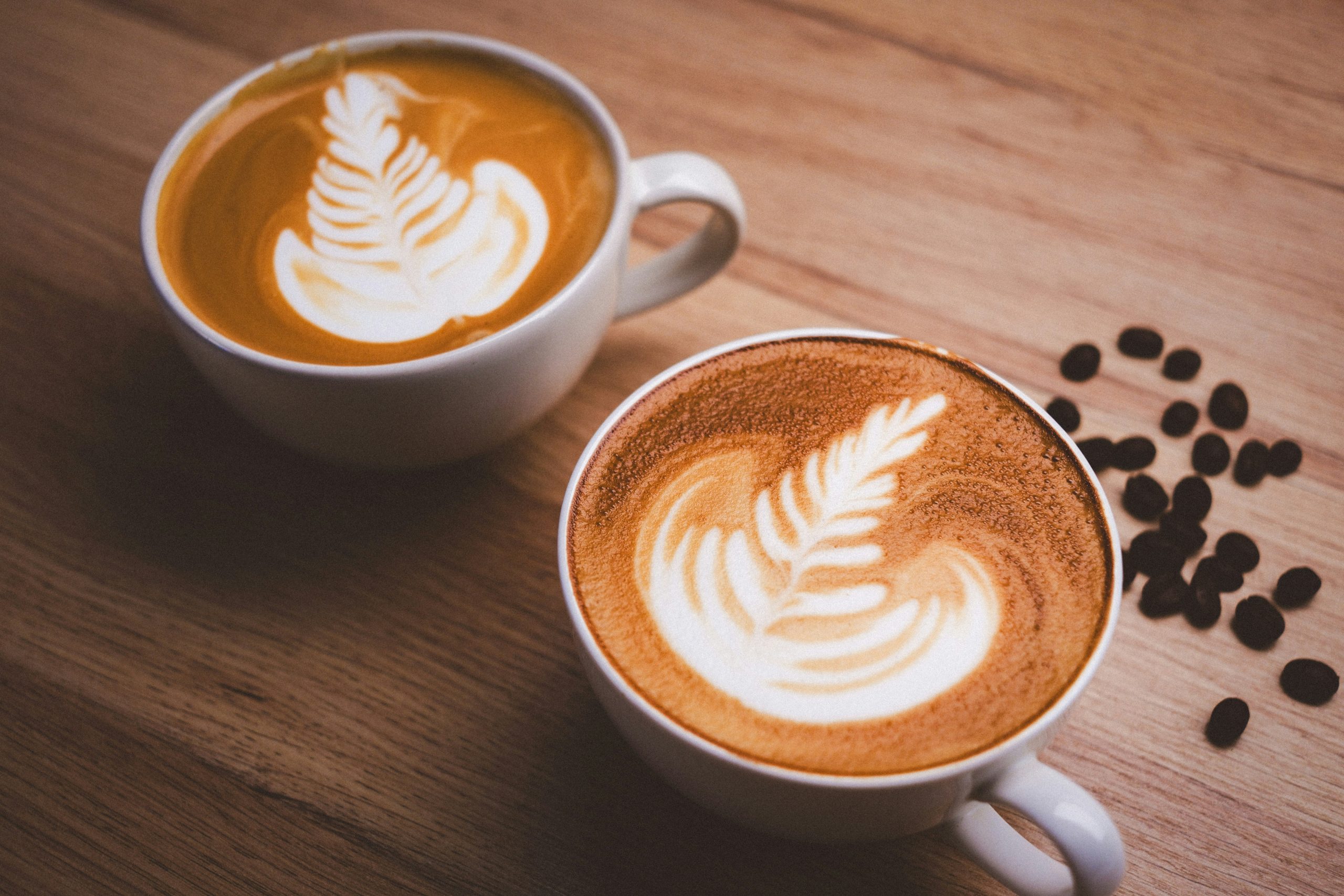 Two cups of latte with pour-over art on a wooden counter — the result a formulation has to repeat every time